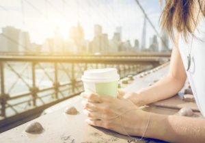 Close up on a woman holding coffee paper cup on Brooklyn bridge in New york