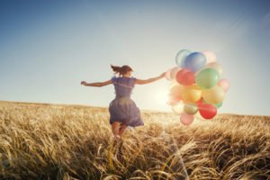 Girl running on the field with balloons at sunset. Happy woman on nature.
