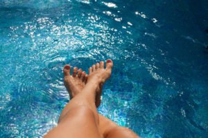 Woman lgs in swimming pool. Tanned feet with pedicure in the pool water.